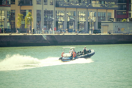 men riding speedboat while treading big canal near building thumbnail