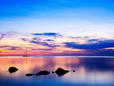silhouette photo of boat and rock in calm body of water at sunset thumbnail