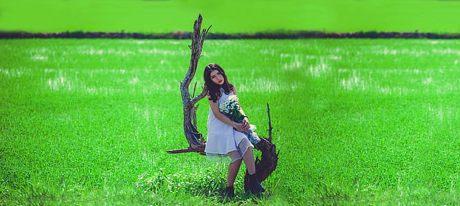Woman in White Sleeveless Mini Dress Holding White Petaled Bouquet Sitting on Gray Tree Branch at Daytime thumbnail