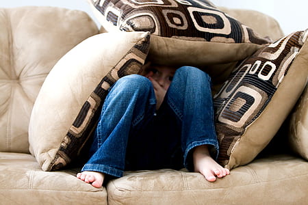 person wearing blue jeans hiding under throw pillows thumbnail