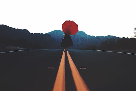 woman wearing black dress walking on black concrete road top while holding red umbrella during daytime thumbnail