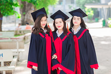 three women wearing black-and-red academic dresses outdoors thumbnail