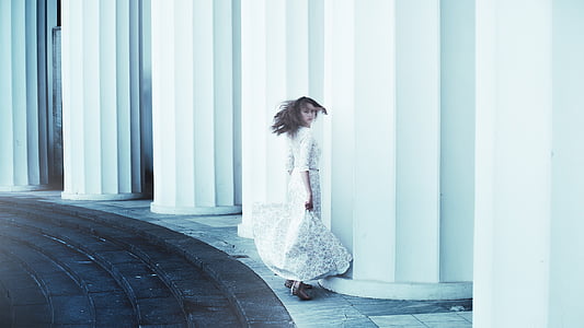 woman in white dress standing beside columns during daytime thumbnail