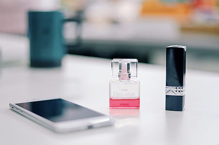 white smartphone beside glass perfume bottle and lipstick thumbnail