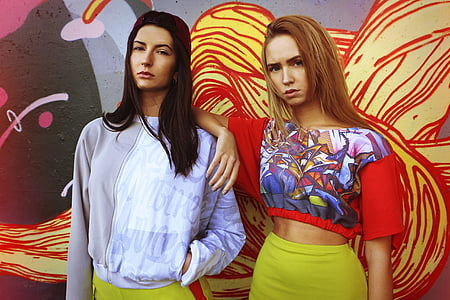 two girls wearing gray and red shirts standing in front of red and yellow wall photo thumbnail