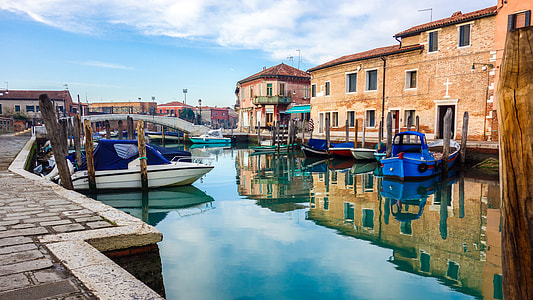 powerboats on river beside docks with concrete houses under cirrus clouds thumbnail