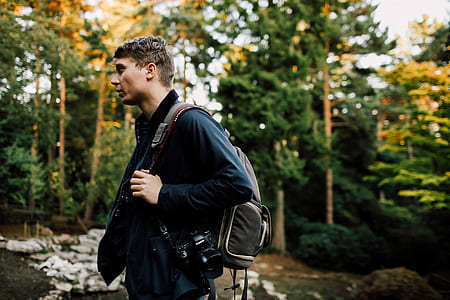 man carrying brown backpack while looking sideways outdoora thumbnail