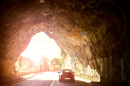 red vehicle on road under rock tunnel during daytime thumbnail