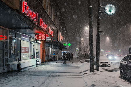 man standing on store facade with snow falling down during nighttime thumbnail