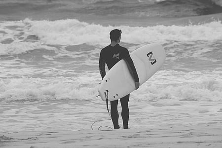 grayscale photography of man carrying surfboard on seashore thumbnail