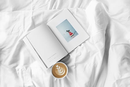 white ceramic mug beside book on white textile thumbnail