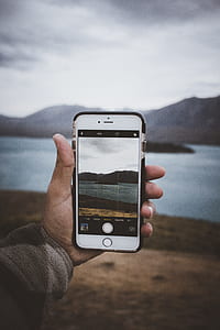 person holding gold iPhone case capturing mountain thumbnail
