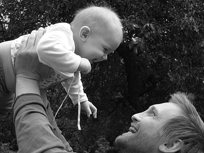 grayscale photo of man lifting baby wearing sweater thumbnail