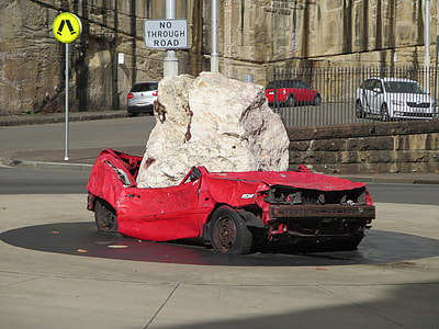 red coupe smashed by gray boulder on gray concrete road thumbnail