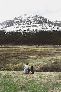 man sitting with dogs looking across snow-capped mountain during daytime thumbnail