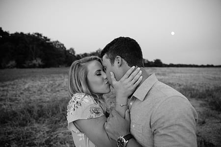 grayscale photo of woman and man kissing on grass field thumbnail