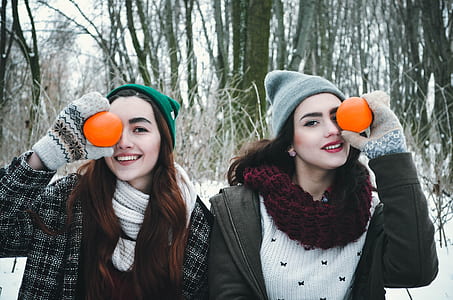 two women holding orange fruits in forest thumbnail