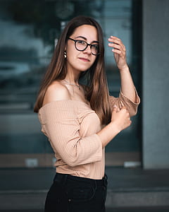 selective focus photography of woman in brown off-shoulder shirt standing near glass wall thumbnail