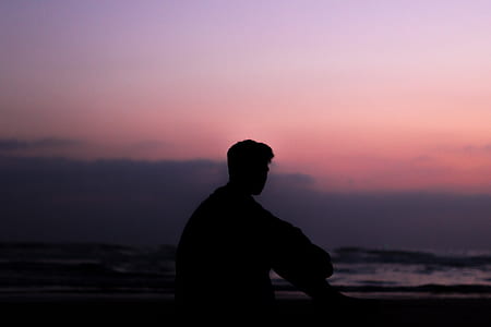silhouette photo of man sitting on seashore thumbnail