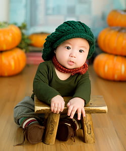 baby wearing green knitted cap, green crew-neck long-sleeved shirt and brown pants sitting near brown stool thumbnail