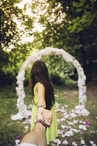 man and woman holding hands walking towards white arch thumbnail