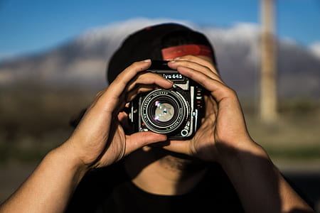 person in black crew-neck t-shirt and black tracker hat using camera during daytime shallow focus photography thumbnail