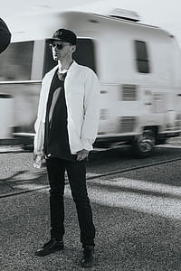gray scale photo of a man in white jacket and black pants standing beside white enclosed trailer thumbnail