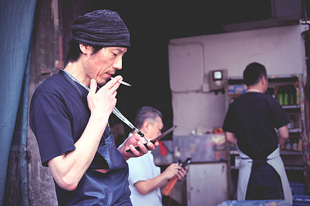man wearing black shirt using flip phone while smoking near two persons standing inside store thumbnail