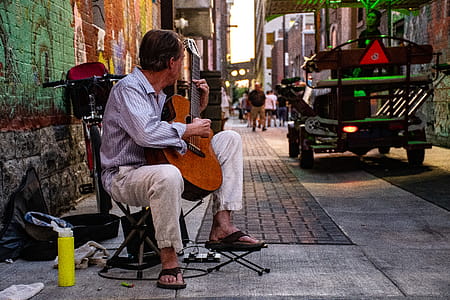 Man Sitting Playing Classical Guitar on Gray Road thumbnail
