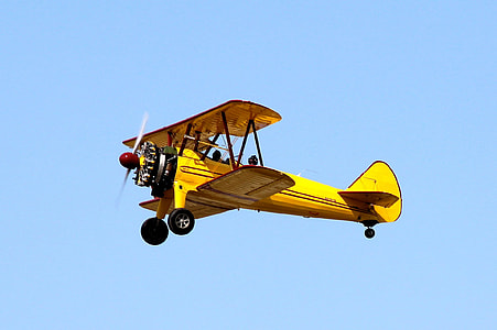 yellow biplane flying under clear blue sky view from ground during daytime thumbnail