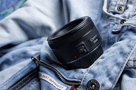 black Canon 50 mm camera lens on blue denim bottoms thumbnail