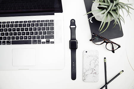 space gray aluminum case Apple Watch with black sports band near black frame wayfarer style eyeglasses and MacBook Pro thumbnail