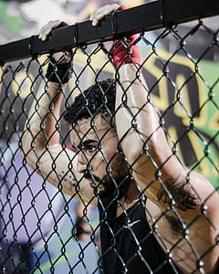 Man Wearing Black Tank Top While Holding Fence thumbnail