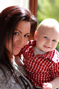 woman with heather gray jacket carrying a baby boy with red-and-white plaid button-up shirt thumbnail