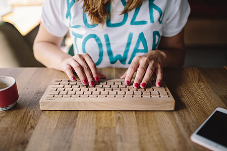 Closeup of female hands typing text on a wireless wooden keyboard thumbnail