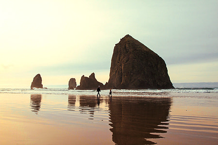man walking on seashore near mountain rock formation during daytime thumbnail