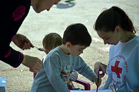 boy in gray long-sleeved shirt holding blue pencil beside woman in white and red crew-neck T-shirt during daytime thumbnail