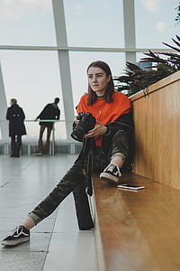 woman holding DSLR camera sitting near wall thumbnail