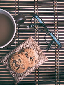 flat lay photography of eyeglasses, mug of coffee and two chocolate chip cookies thumbnail