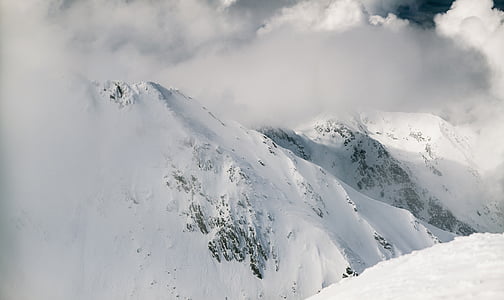 snow covered mountain surrounded by fogs under white cloudy sky at daytime thumbnail