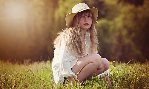girl sitting on green grass surrounded by green leafed trees thumbnail