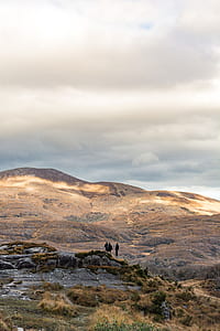 three person on rock near mountain under white cloudy sky thumbnail