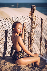 woman in black and brown floral bikini sitting on beach shore during daytime shallow focus photography thumbnail