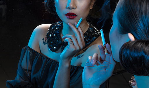 woman holding lighted cigarette stick in front of mirror thumbnail