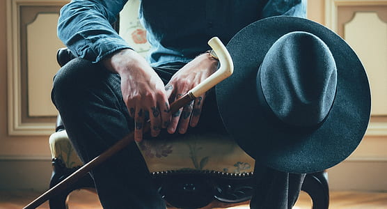 person holding brown wooden cane and black fedora hat thumbnail