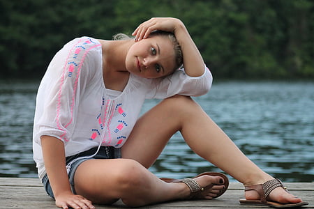 woman wearing white and pink crew-neck elbow-sleeved blouse sitting on brown wooden dock near green leaf trees during daytime thumbnail