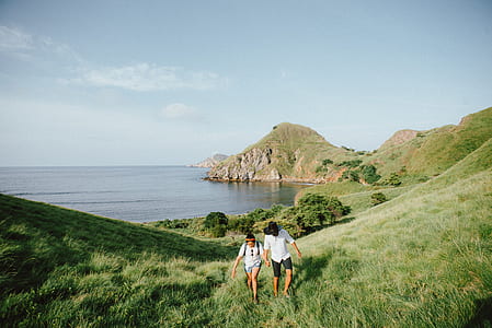 man and woman walking on hill surrounded with ocean during blue hour thumbnail