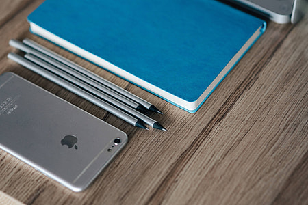 Silver iPhone with a blue notebook and pencils thumbnail