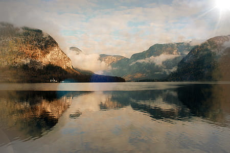 body of water surrounded by mountain under calm sky thumbnail