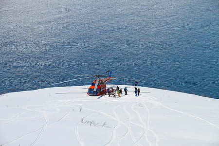 helicopter landed on snow covered mountain near body of water thumbnail